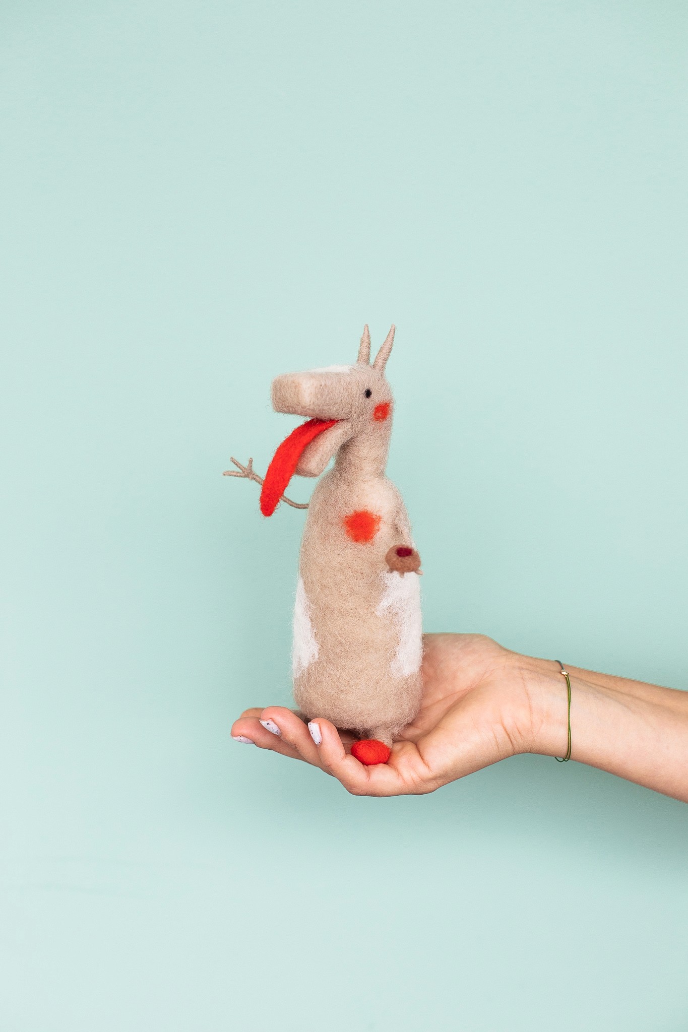 Béžová postava turoňa z vlny so silným červeným jazykom a oranžovými bodkami.