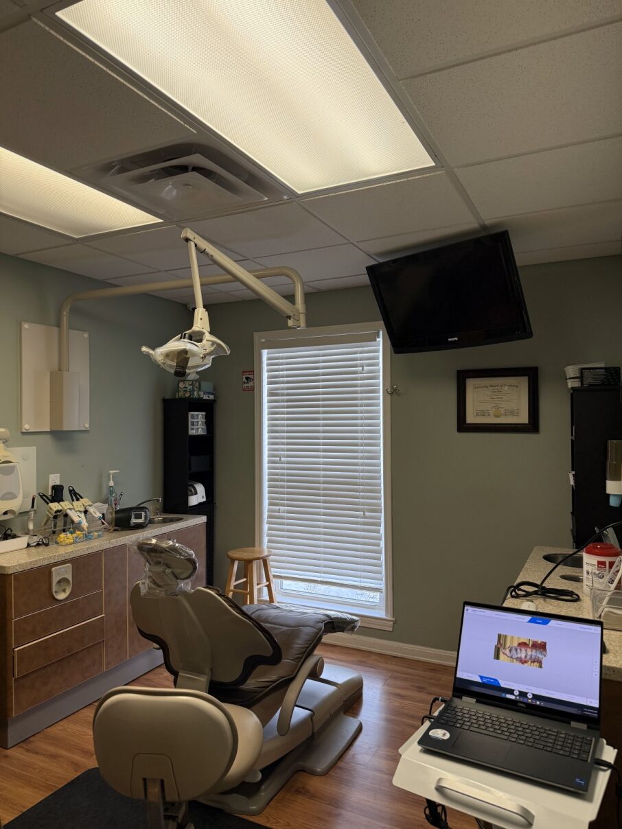 Professional dental exam room featuring a modern patient chair, overhead operatory lighting, and digital diagnostic equipment.