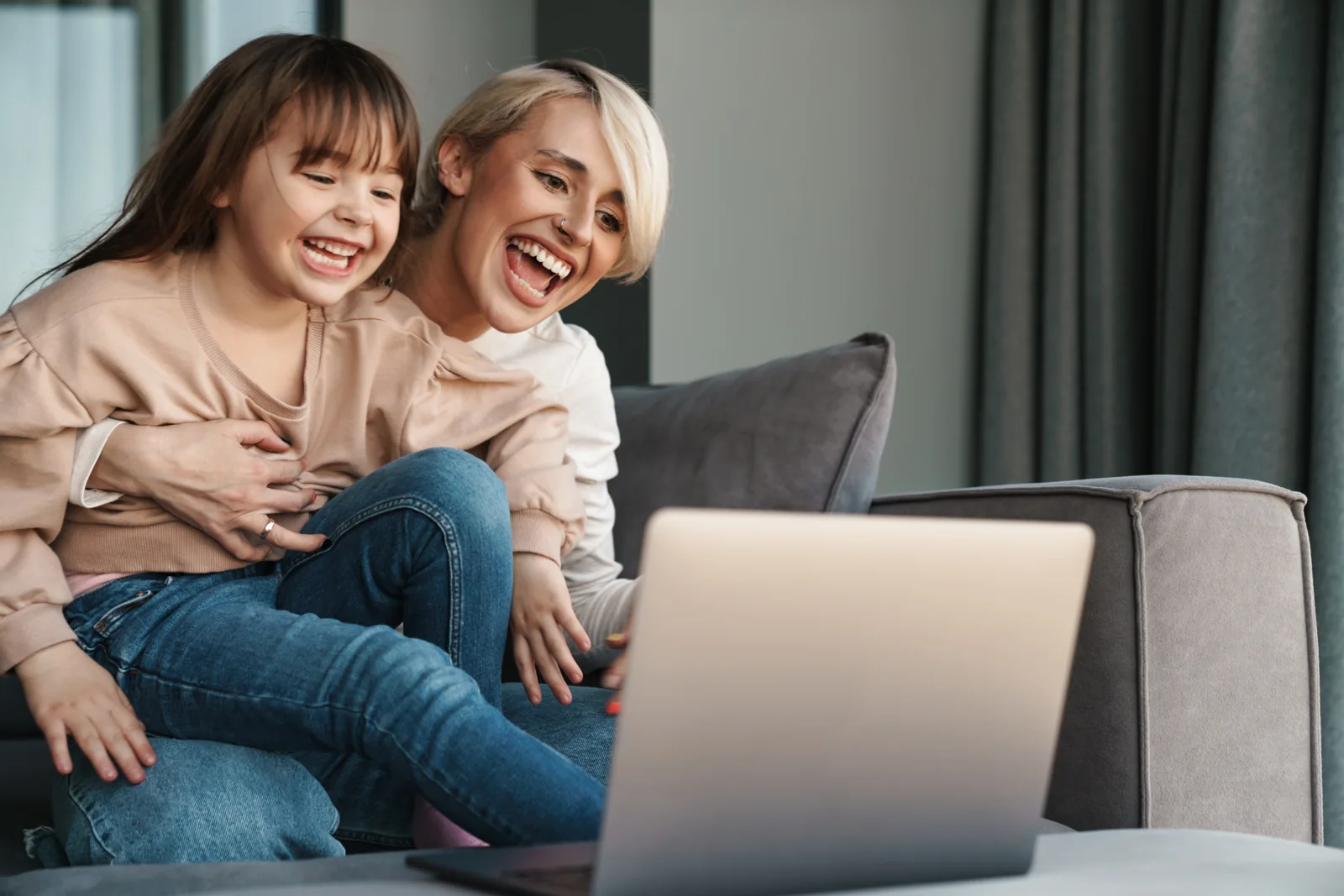 Mother and daughter laughing together beside a laptop at home