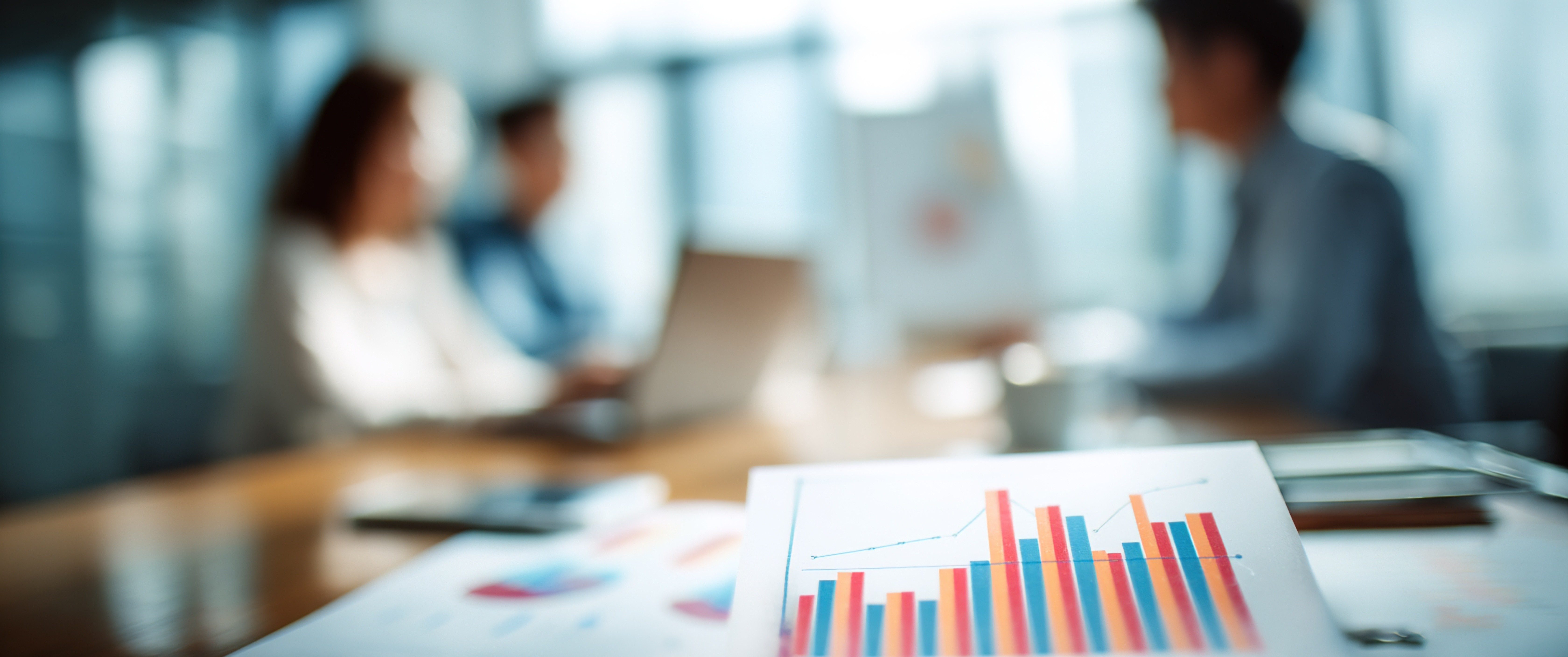Close-up of charts on a desk with blurred professionals working in the background
