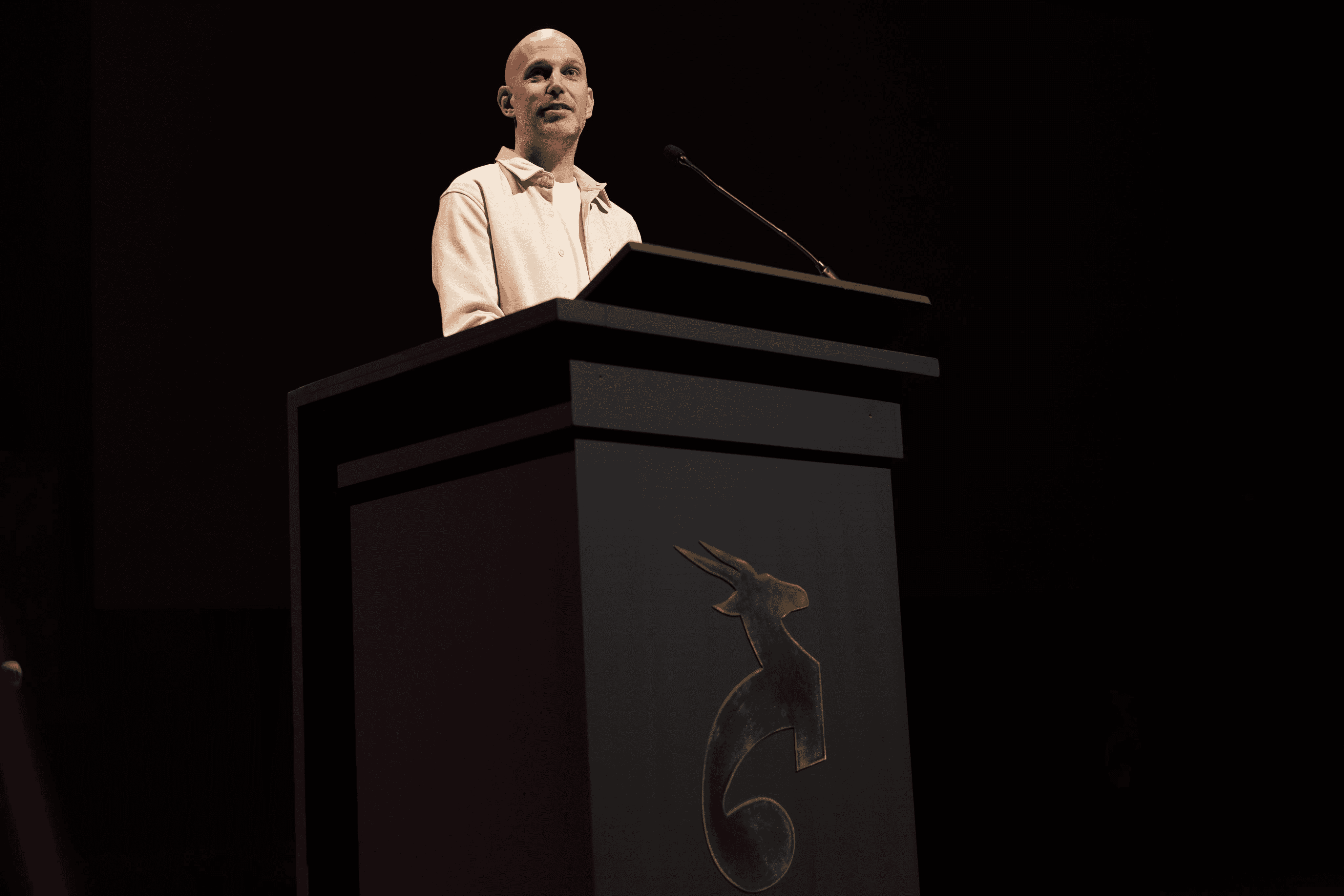 A woman wearing black rain gear and a backpack smiles as she walks down a dirt trail followed by a black dog, with mountains and a body of water in the background.