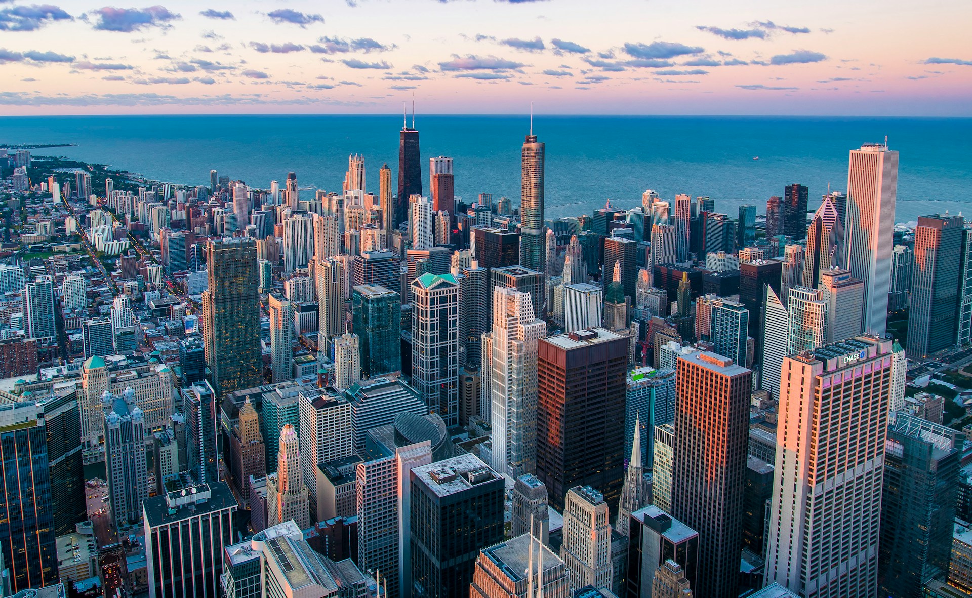 Aerial view of Chicago's dense downtown skyline with Lake Michigan in the background at dusk.