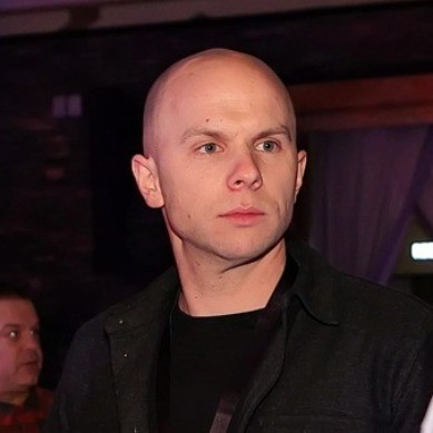 A woman with long dark hair wearing a black hijab, looking calmly at the camera against a muted background.