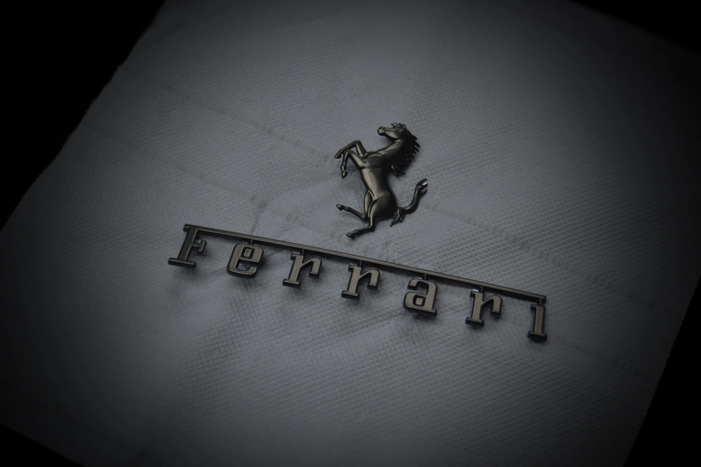 Schwarzes Ferrari-Pferdeemblem und Ferrari-Schriftzug bei AT Plus.
