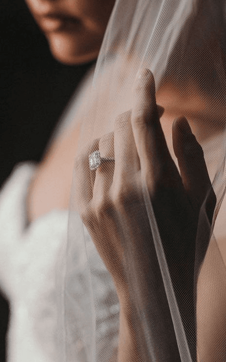 Elegant detail shot of a bride’s ringed hand beneath a sheer veil, reflecting the understated elegance characteristic of fine art wedding photography.