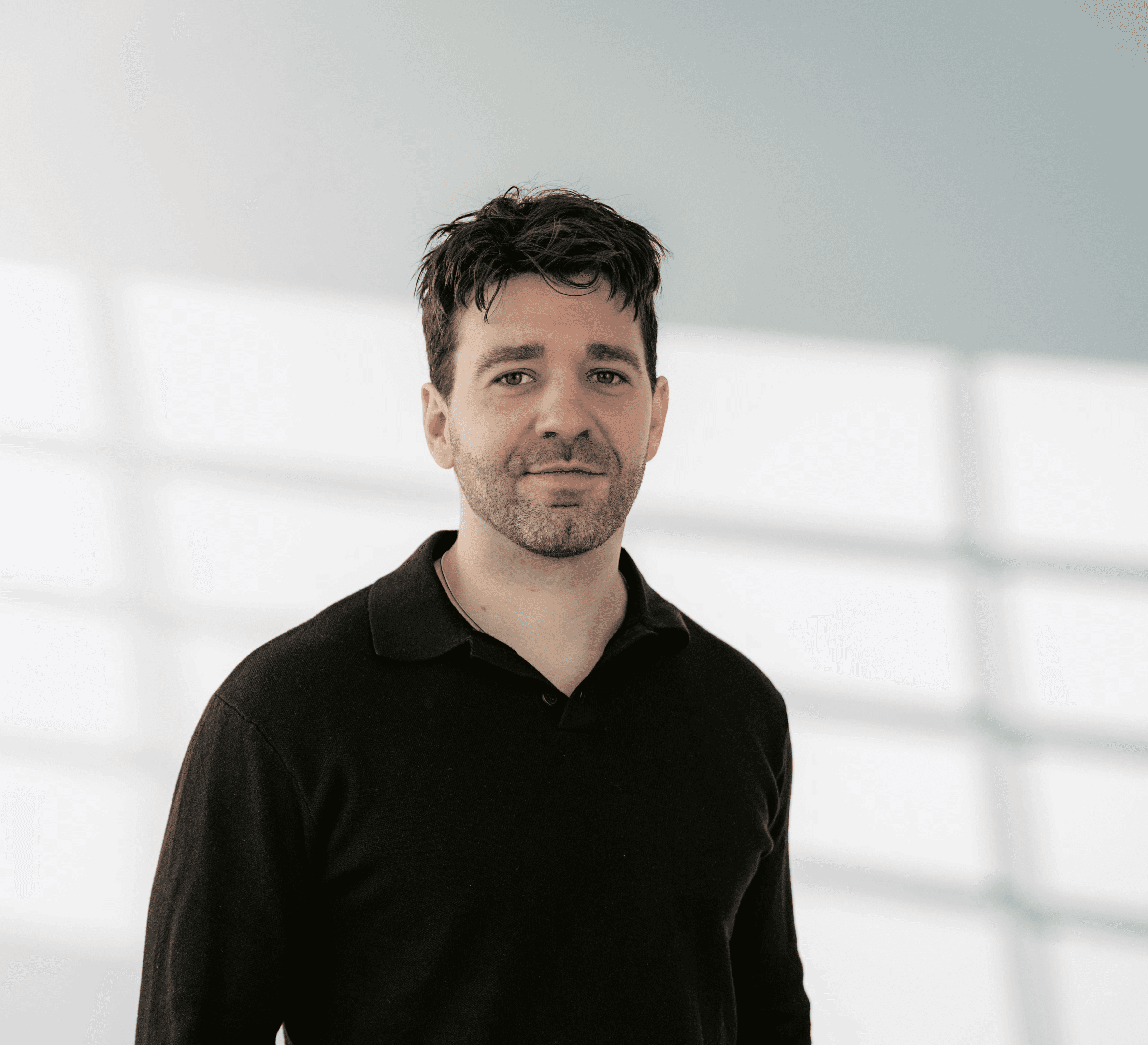 Ein Junger Mann mit schwarzem Pulllover und Hände in der Tasche blickt freundlich in die Kamera.