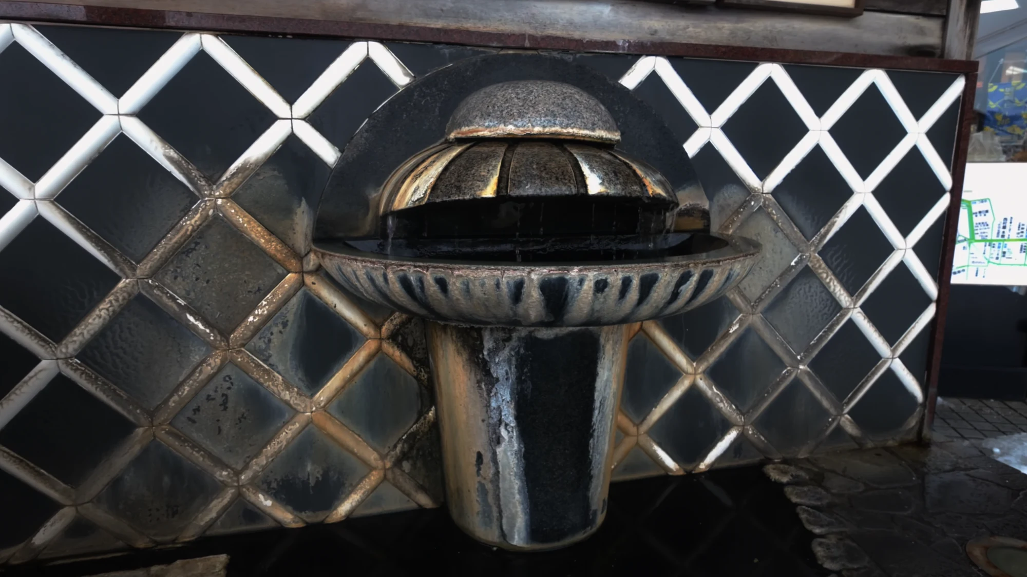 A stone hot spring drinking basin lit from above against a lattice screen at night.