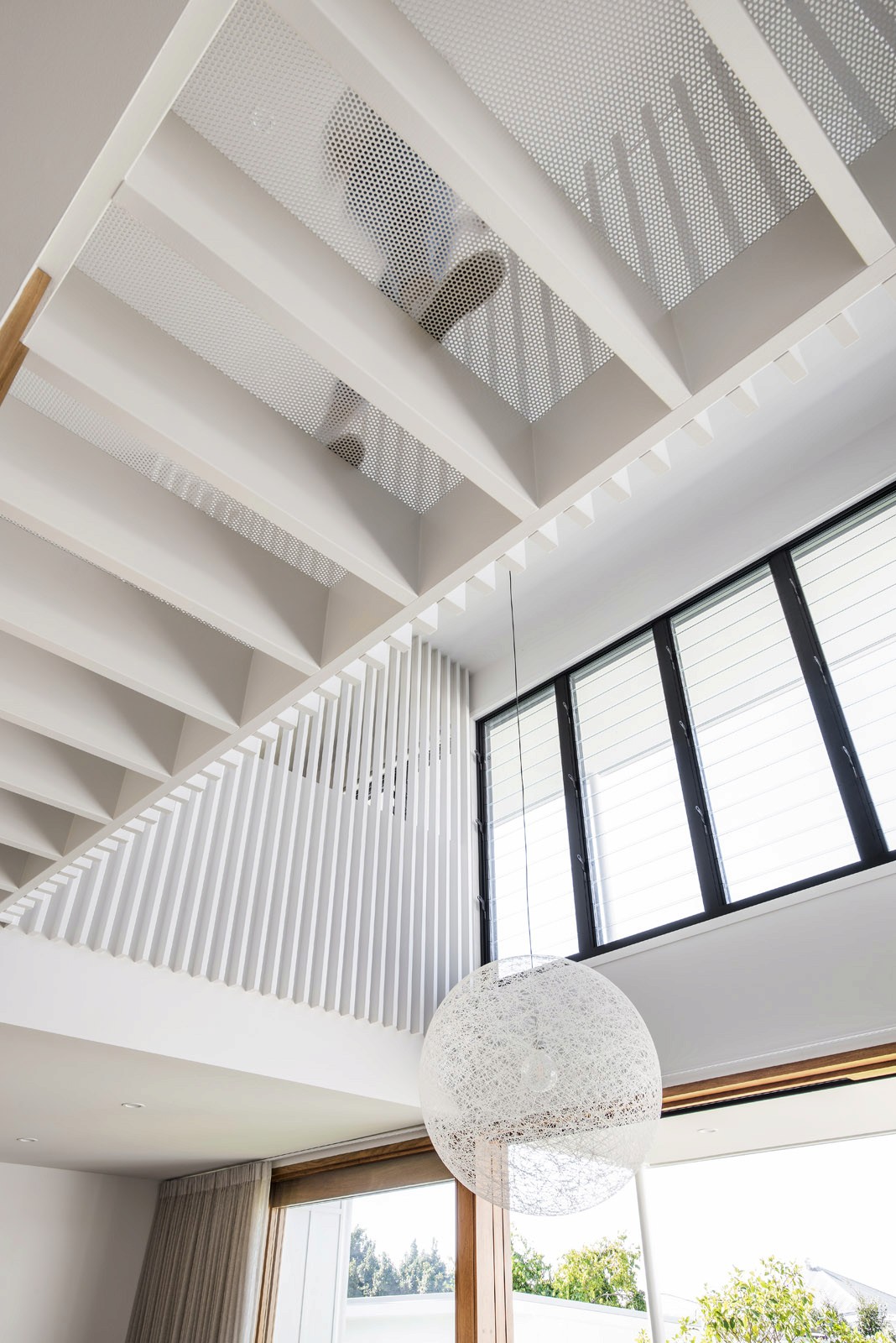 Interior ceiling detail with exposed beams, perforated panels, high windows, and pendant light