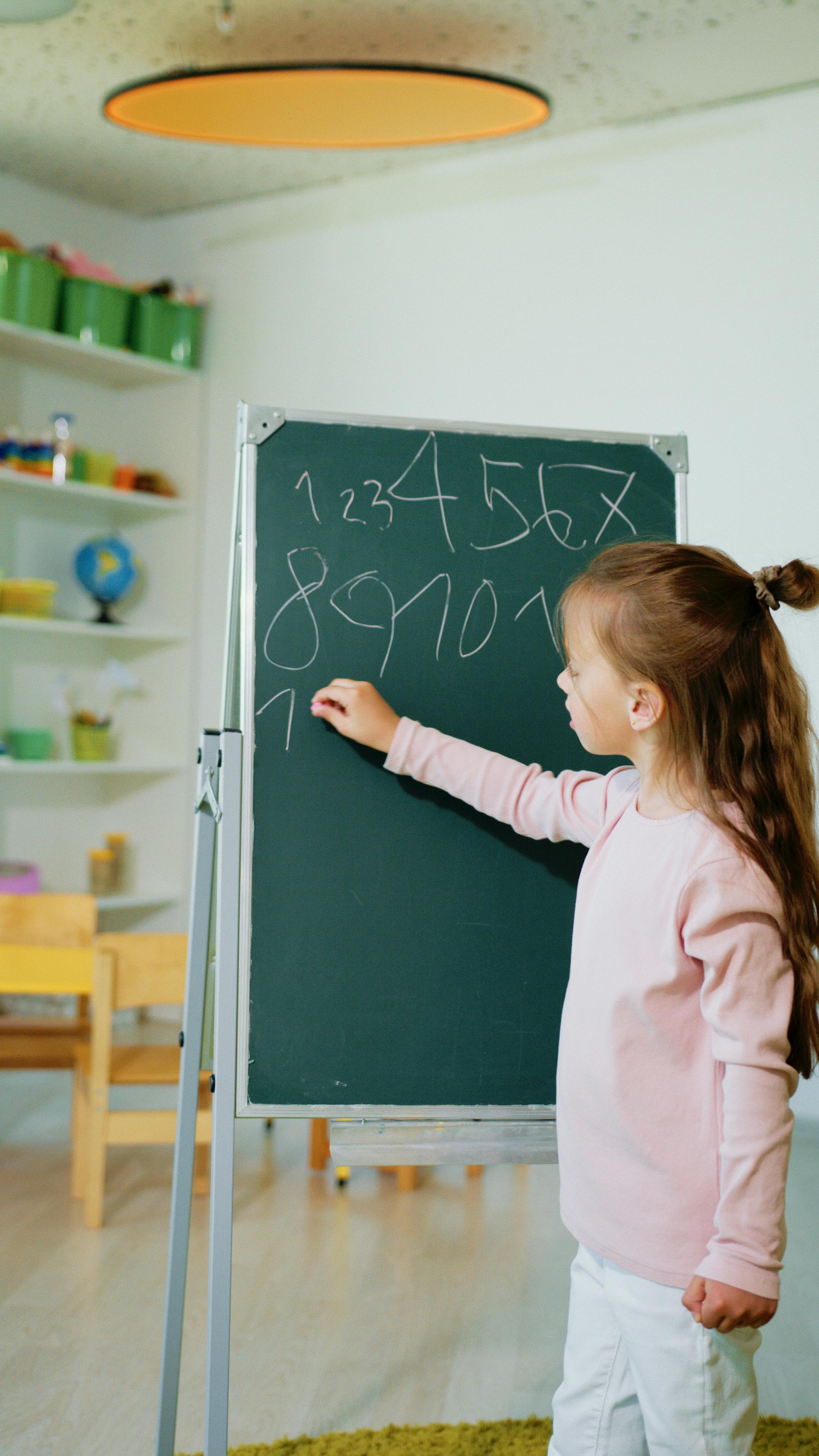 En flicka skriver med krita på en grön tavla