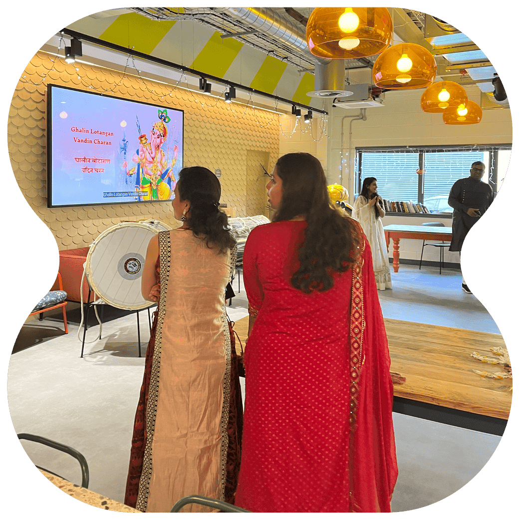 People wearing traditional clothing viewing a display screen with cultural artwork and text in an event space decorated with warm lighting.