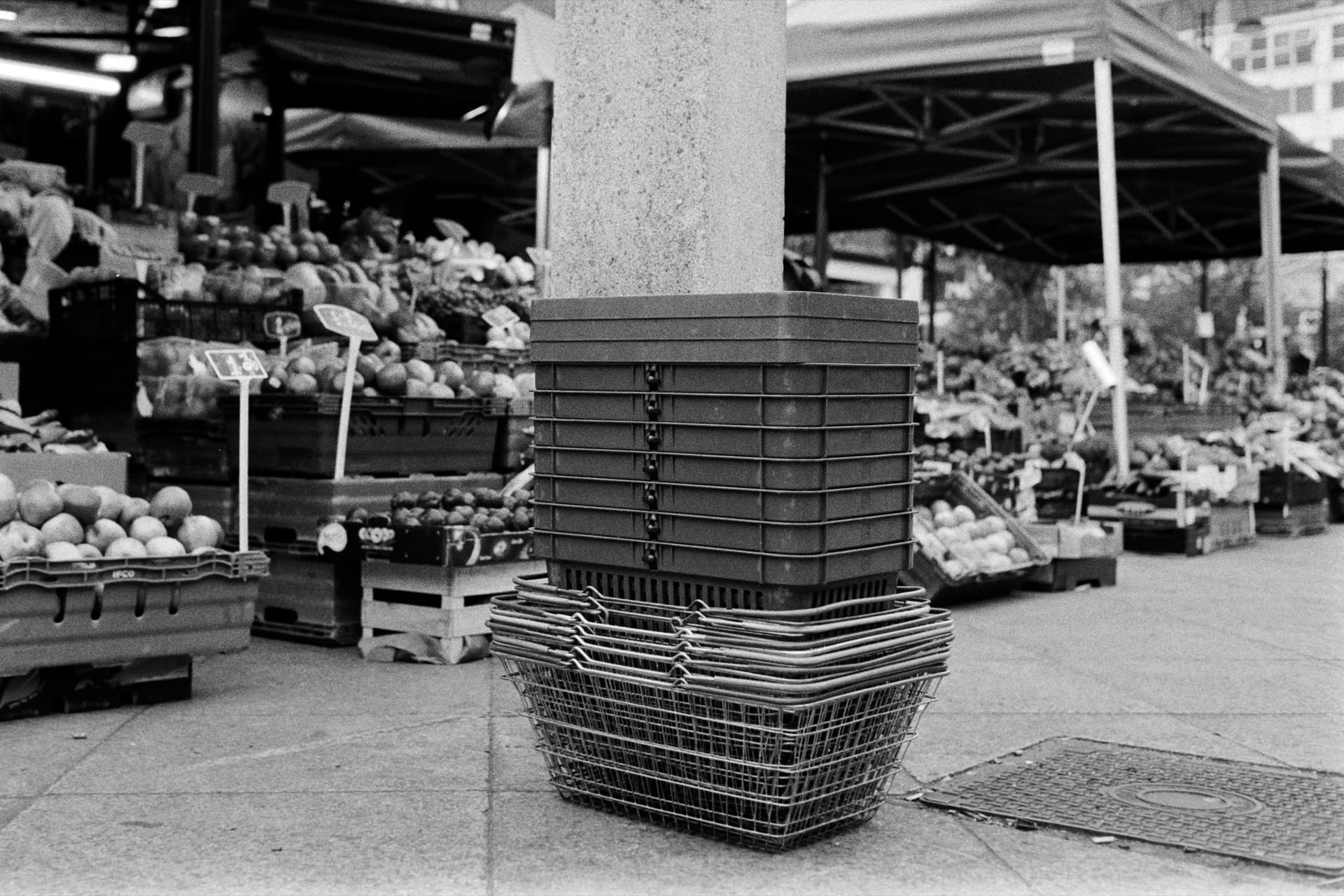 Stacked plastic crates wrapped around concrete pillar at outdoor market with produce displays