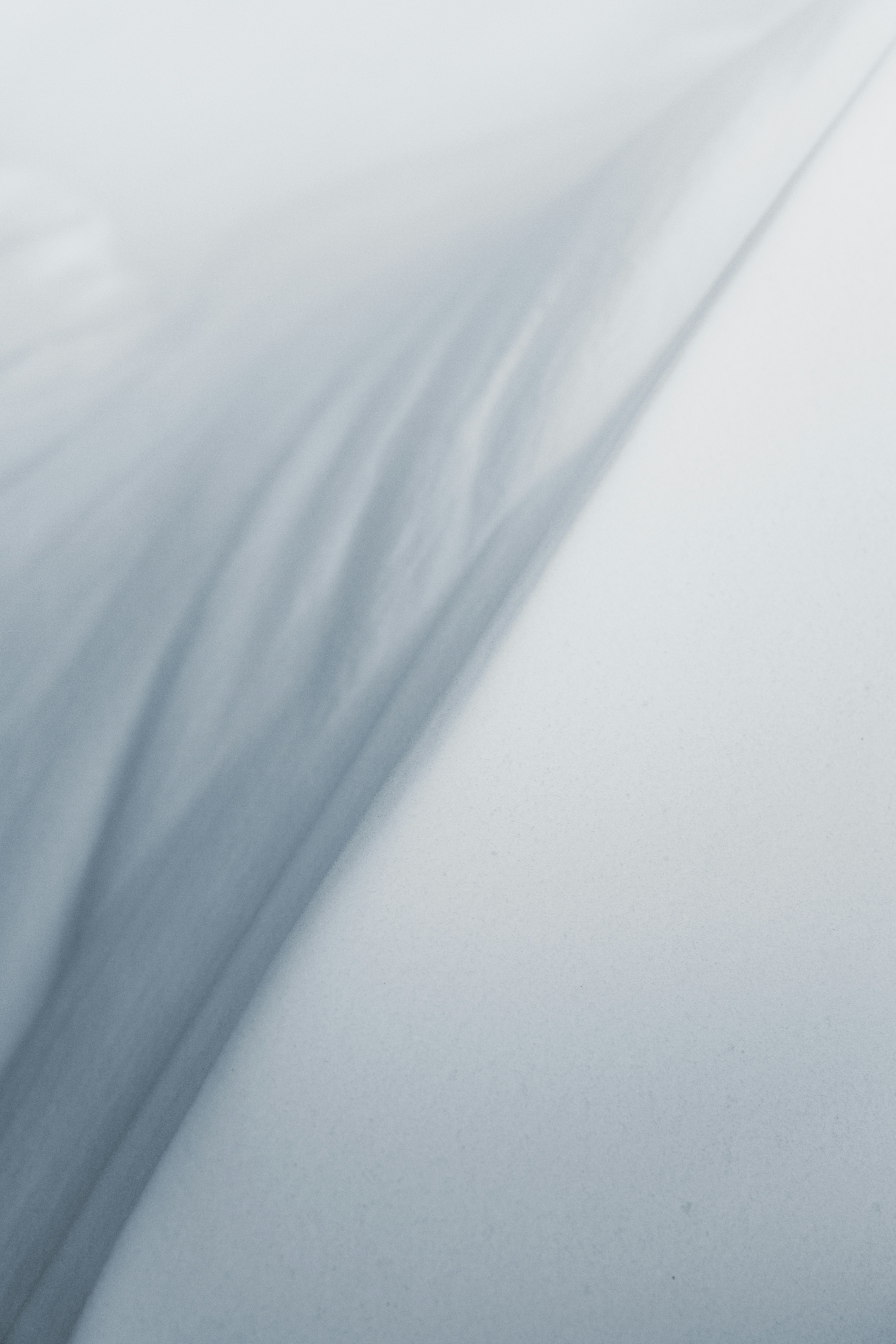 Close-up portrait of a person wearing a gray insulated hooded jacket with the hood up, showing their face framed by the hood against a light background.