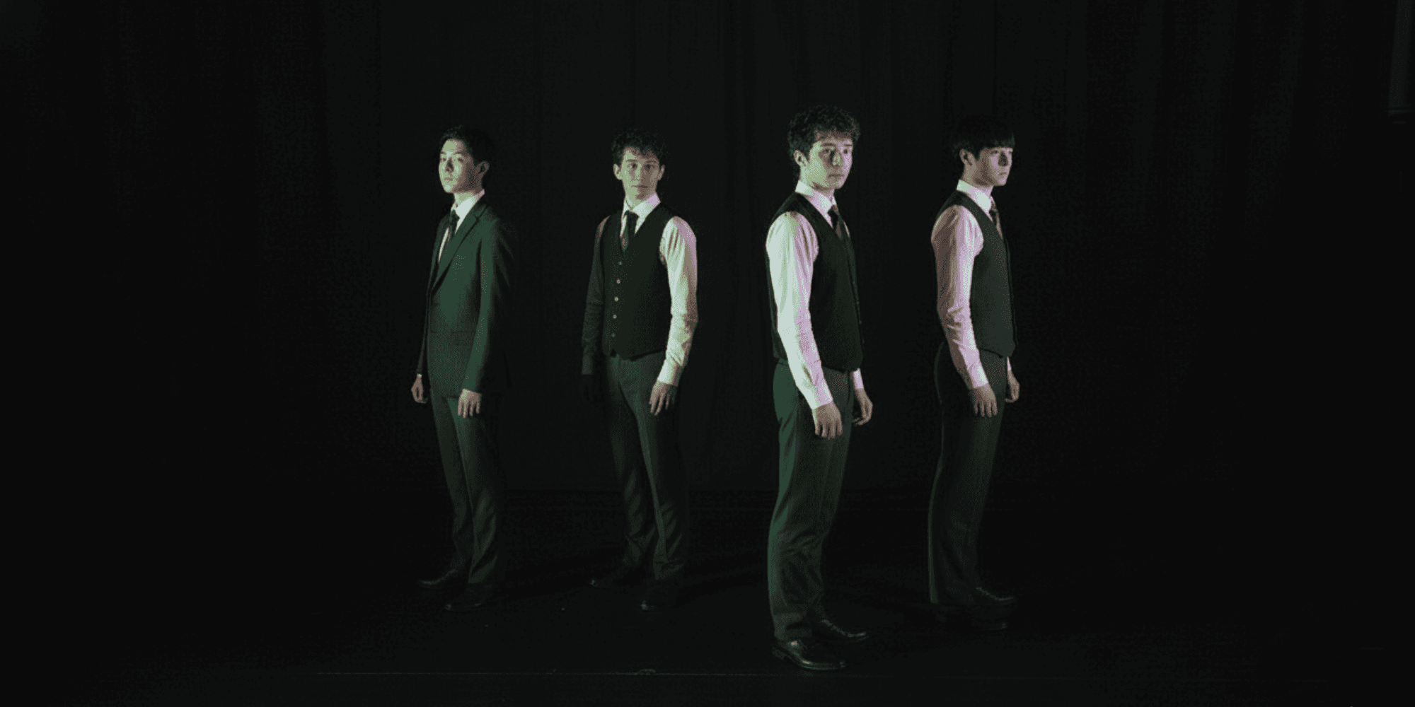 大学の演劇サークルで4人が舞台衣装を着て暗い背景の前に立つ写真