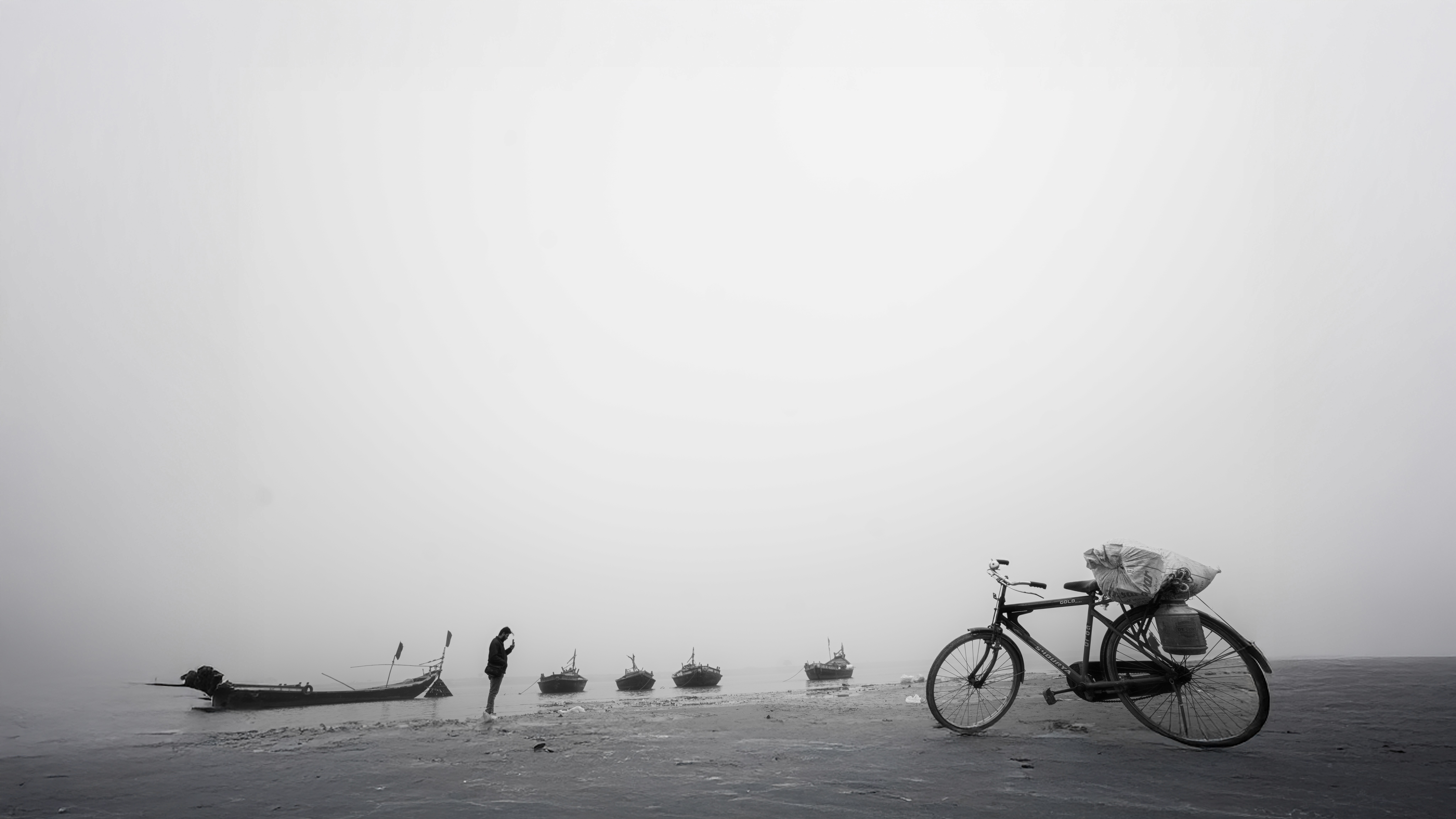 Person wearing black clothing carrying a black tote bag with a green globe-like geometric symbol, standing against a concrete wall in sunlight and shadow.