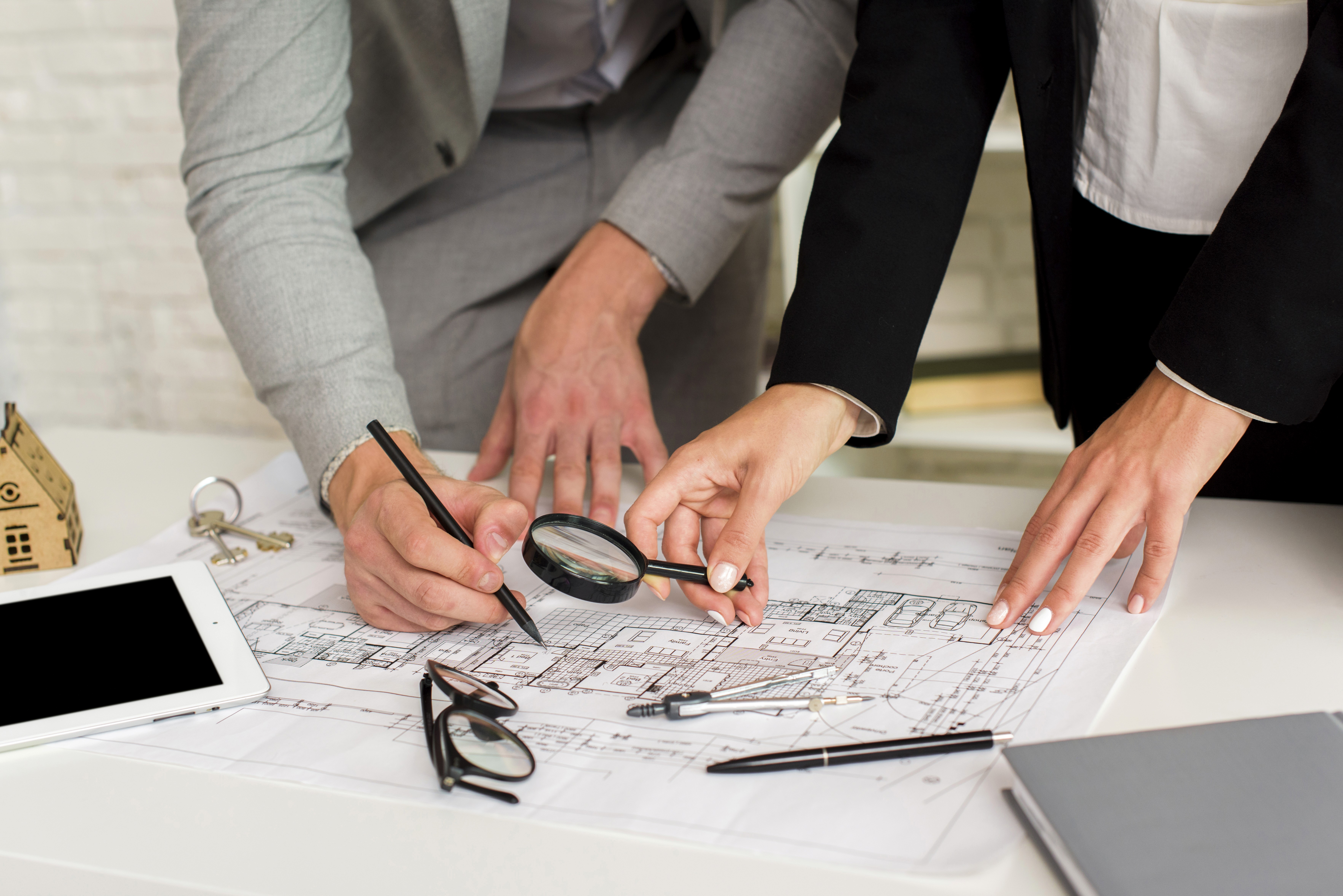 Close-up of hands working together on documents and plans, with pens and a smartphone visible on a desk.