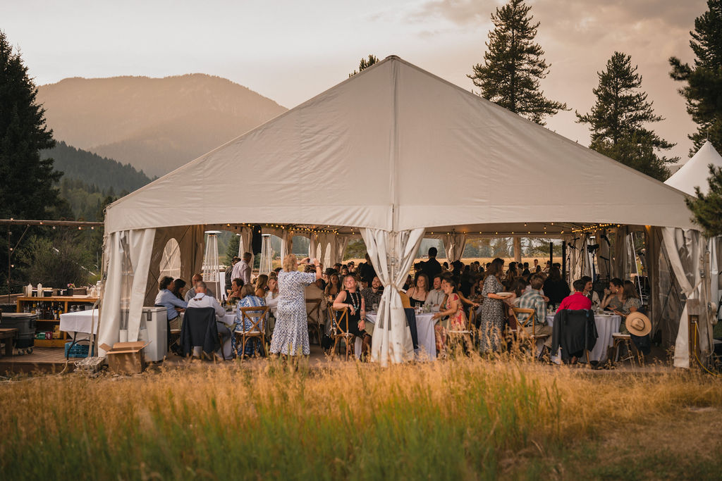 Wedding reception tent glowing at dusk in a mountain meadow