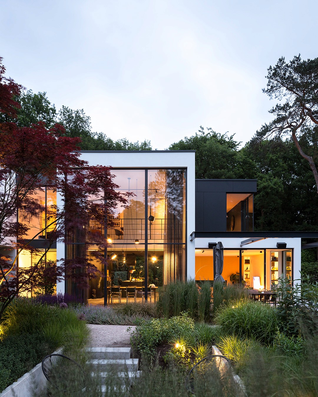 Moderne vrijstaande villa met houten gevelbekleding, grote ramen en verlichte entree tussen het groen