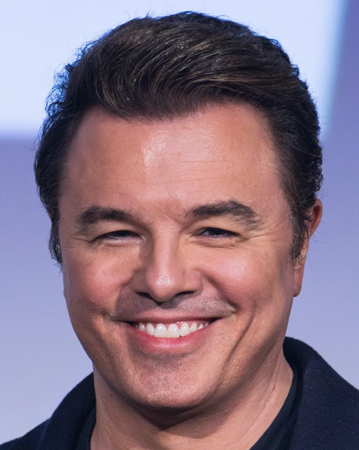 Head shot of a man with brown hair smiling confidently at the camera, in front of a blurred background.