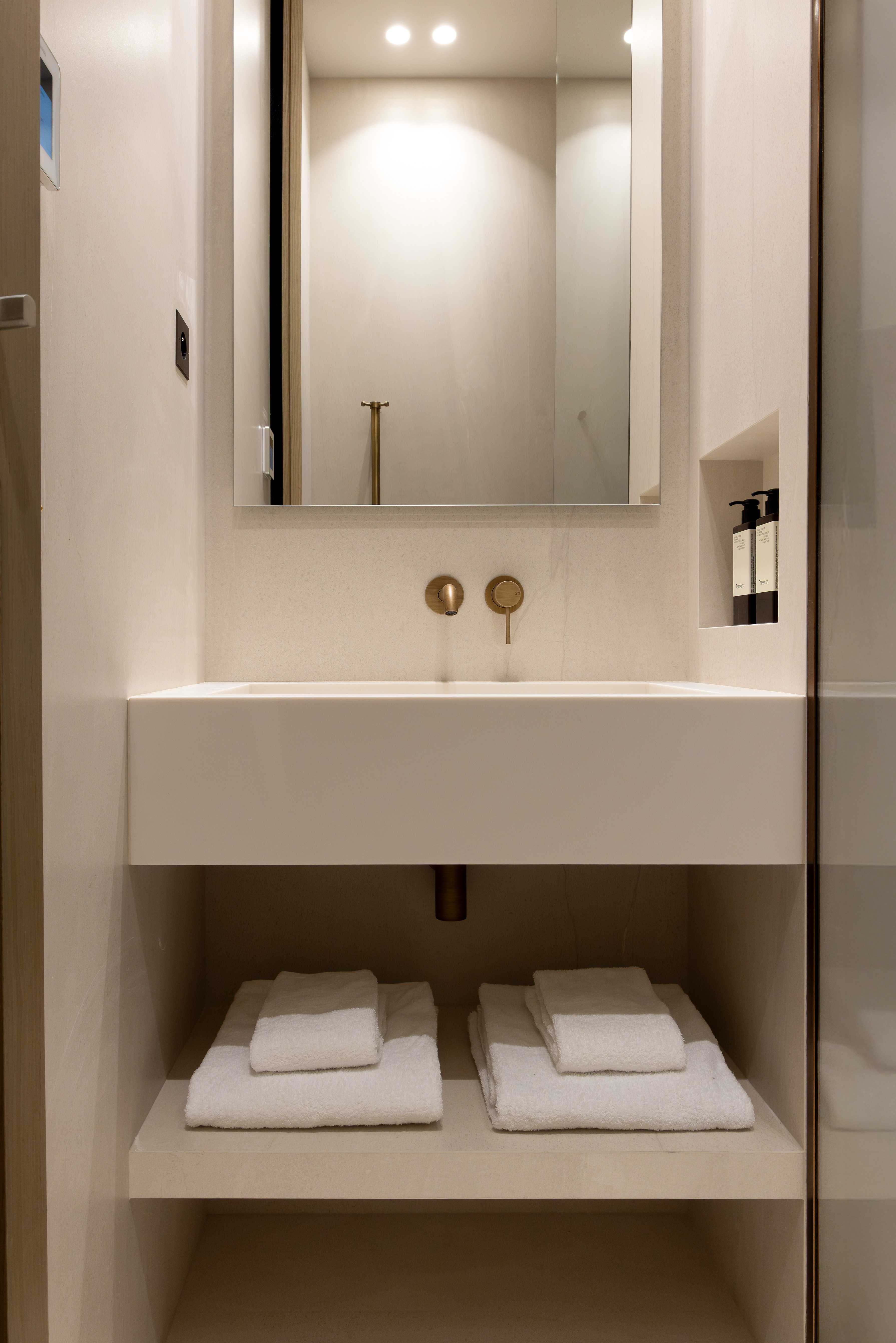 Salle d'eau avec vasque suspendue, robinetterie doree, miroir eclaire, serviettes blanches rangees en dessous
