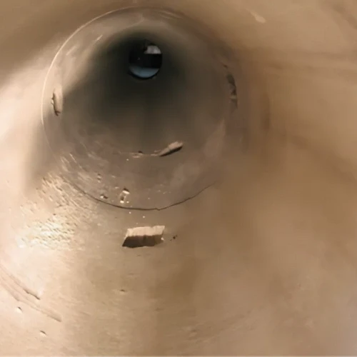 Ein Blick ins Innere eines Metallrohrs mit verschiedenen Kratzern und Unregelmäßigkeiten. Dunkle Öffnung am Ende.