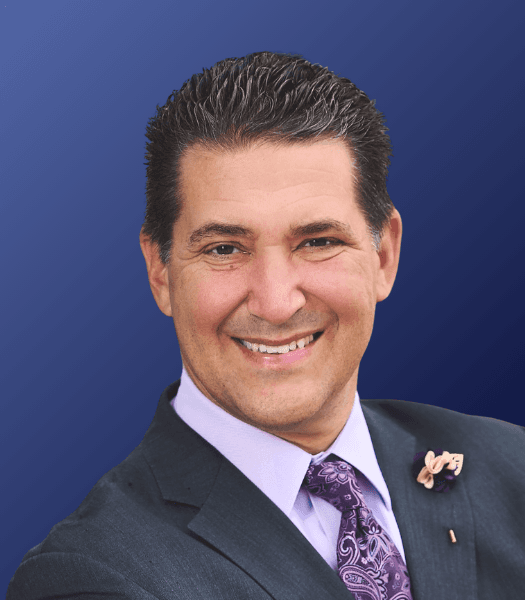 Anytime AI co-founder John Blake wearing grey suit with purple shirt and tie, smiling at camera