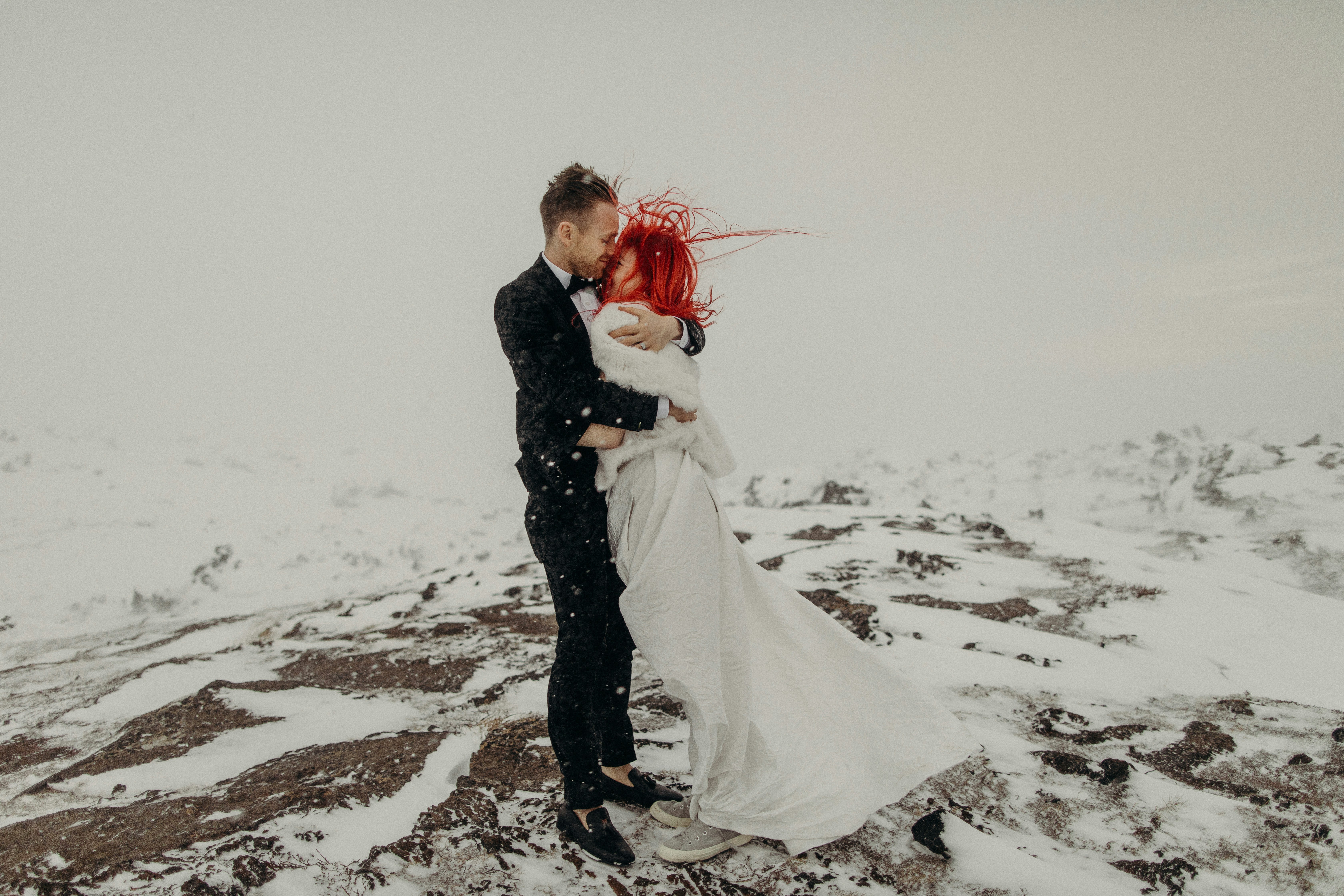 a bride and groom standing on top of a snow covered mountain
