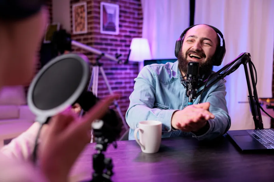 Podcastsetup mit violetter Beleuchtung. Zwei Menschen nehmen ein Gespräch auf und lachen.