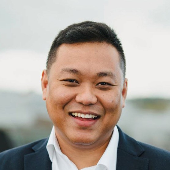 A woman with short curly hair wearing a black t-shirt looks into the camera.