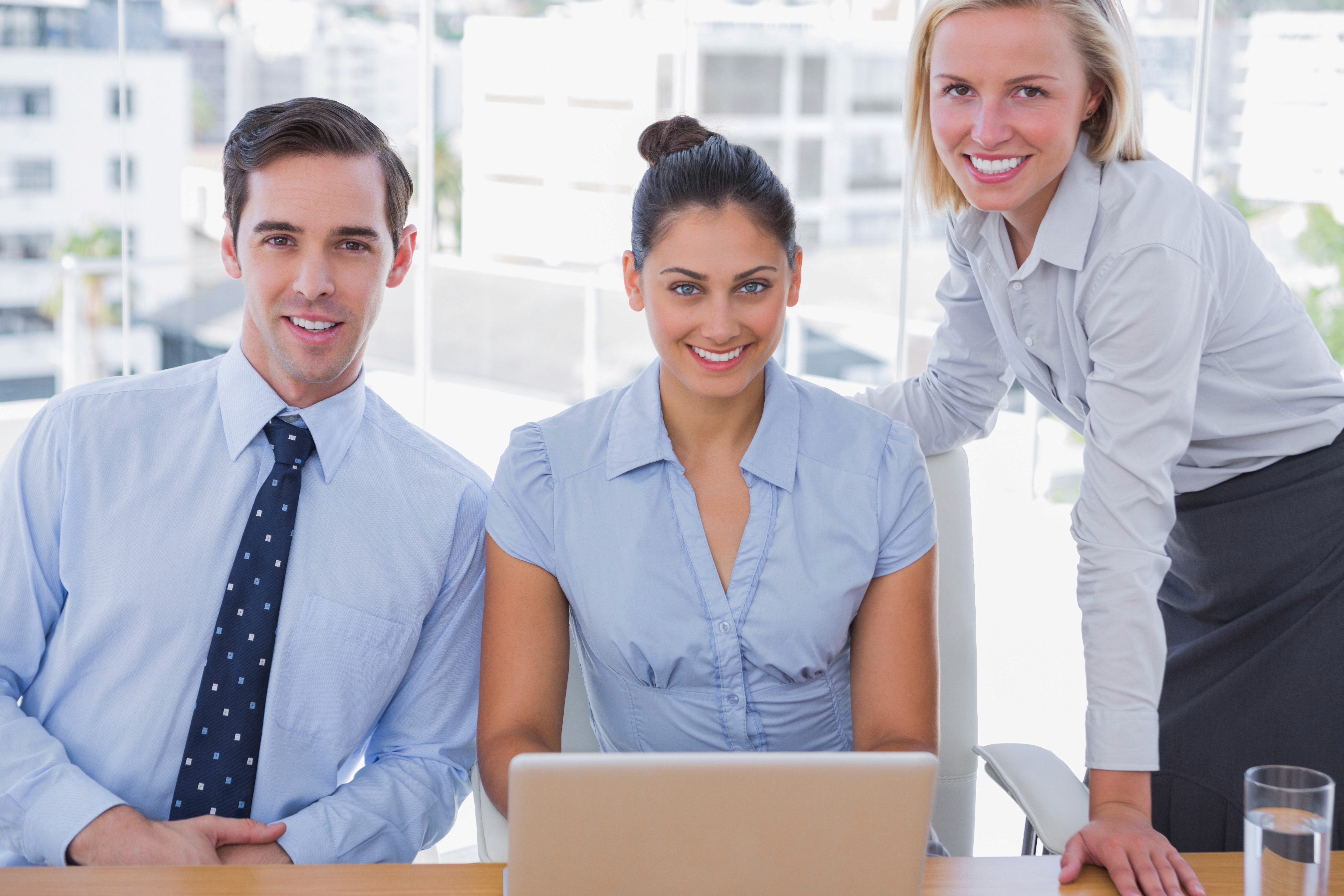 Three women in a collaborative meeting, with one blonde woman smiling and gesturing while discussing ideas, and a tablet displaying a video conference