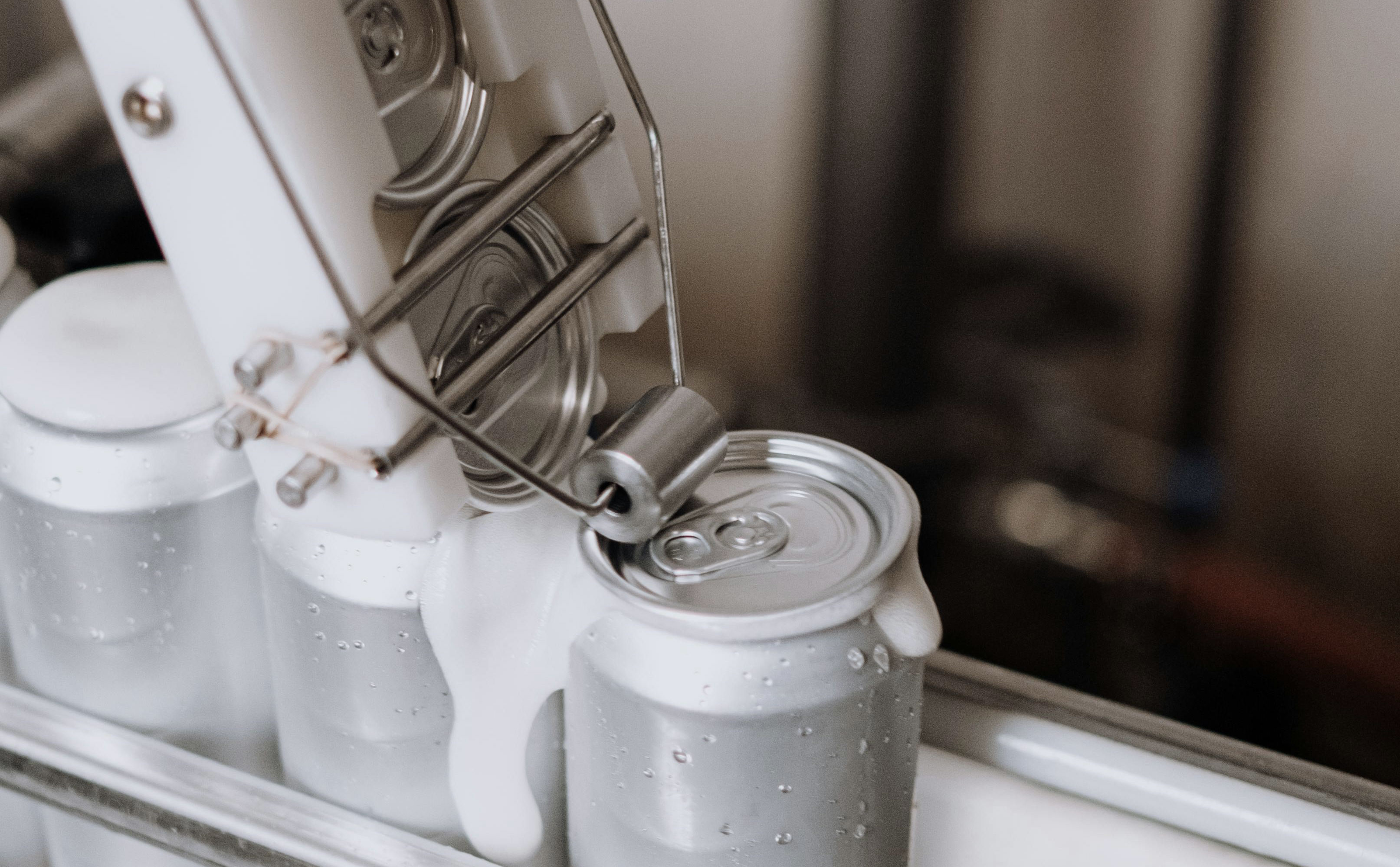 A close-up of an automated can sealing machine, with several cans lined up on a conveyor system.
