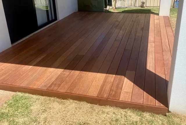 Timber decking beside a home, with a finished edge above the lawn.