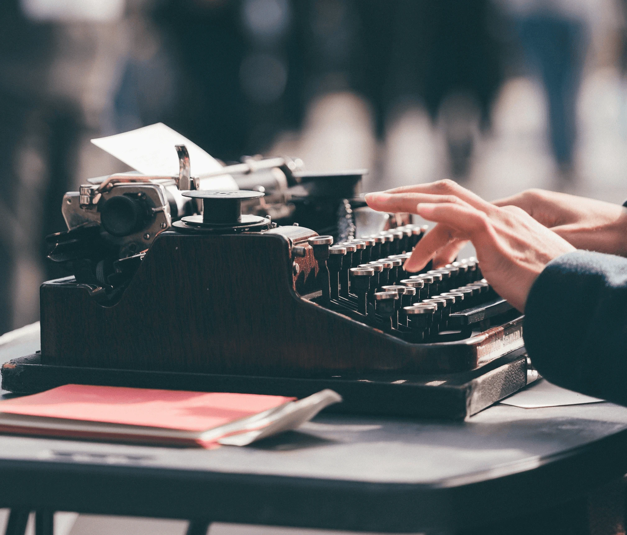 Alte Schreibmaschine im Freien mit Händen beim Tippen, verschwommener Hintergrund.