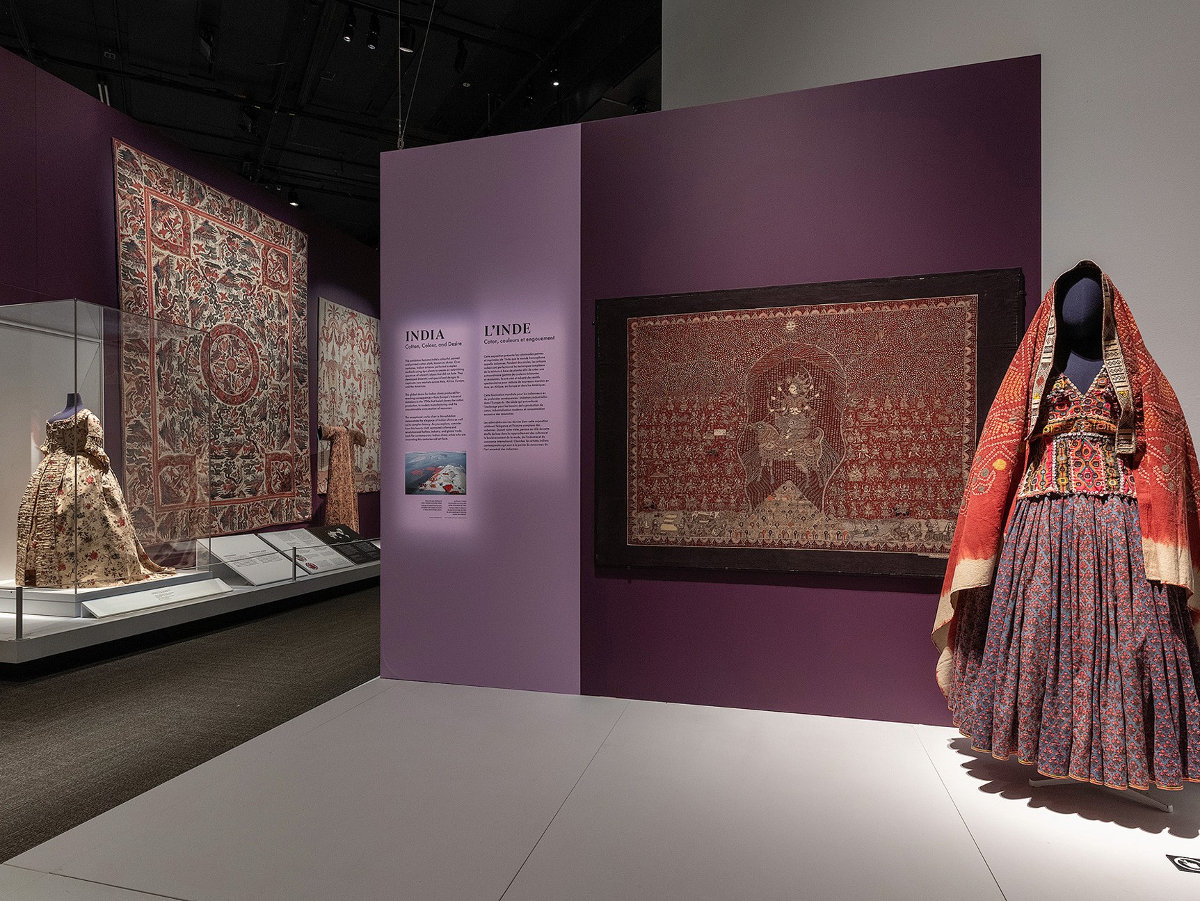 View of an exhibition space featuring mannequins draped in elaborately decorated textiles in purple, red and gold