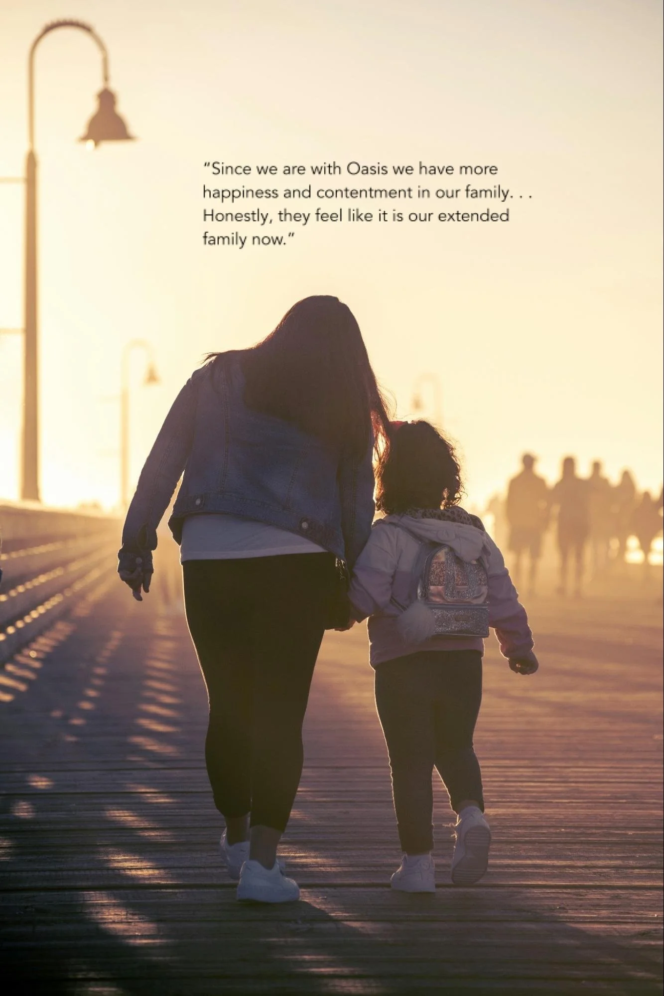 Uma mulher e uma criança de mãos dadas caminham por um calçadão ao pôr do sol, com postes de luz e silhuetas de pessoas ao fundo enevoado, acompanhadas por uma citação emocionante sobre felicidade e contentamento em família.