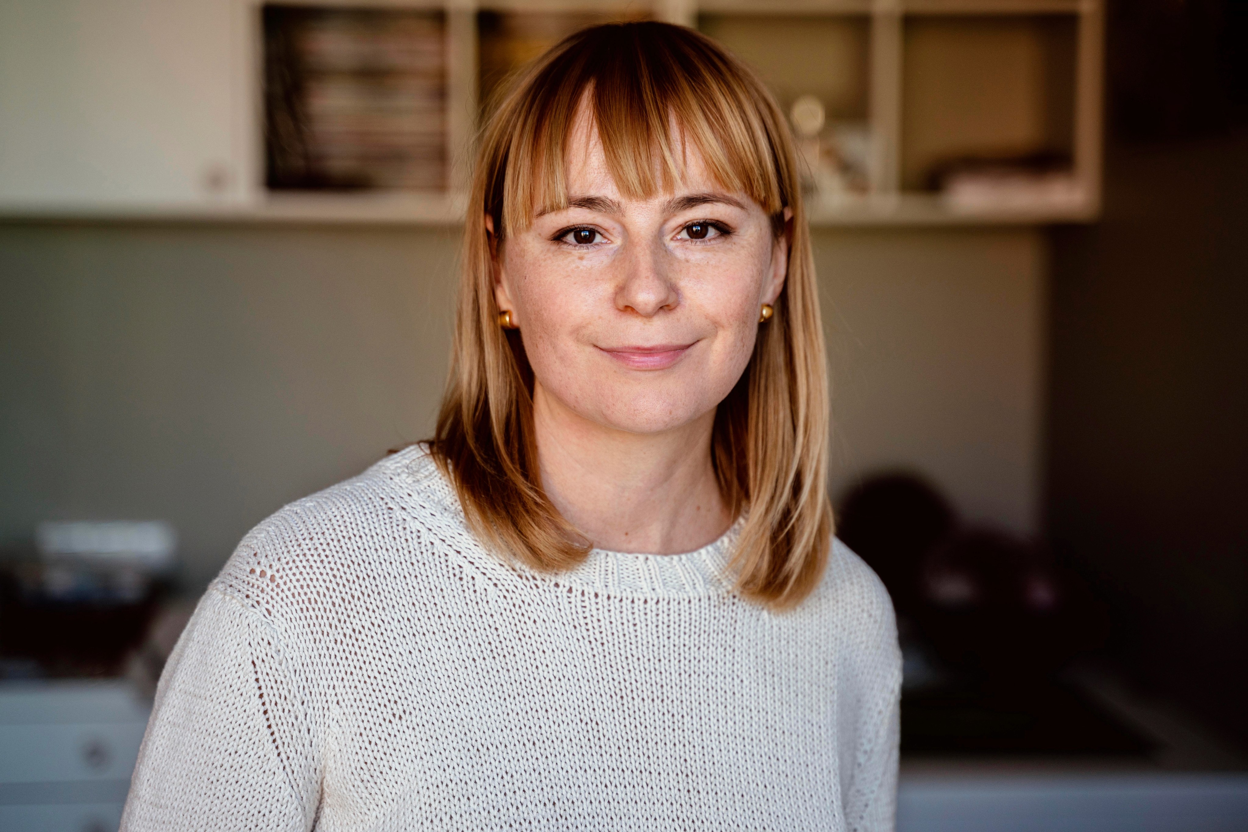 Portrait of a woman with blonde hair wearing a white sweater, smiling directly at the camera. 
