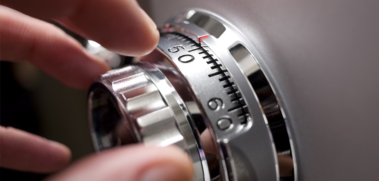 Close-up view of a man's hand dialing a 'spy-proof' safe dial, where numbers are visible only at the top, enhancing security.