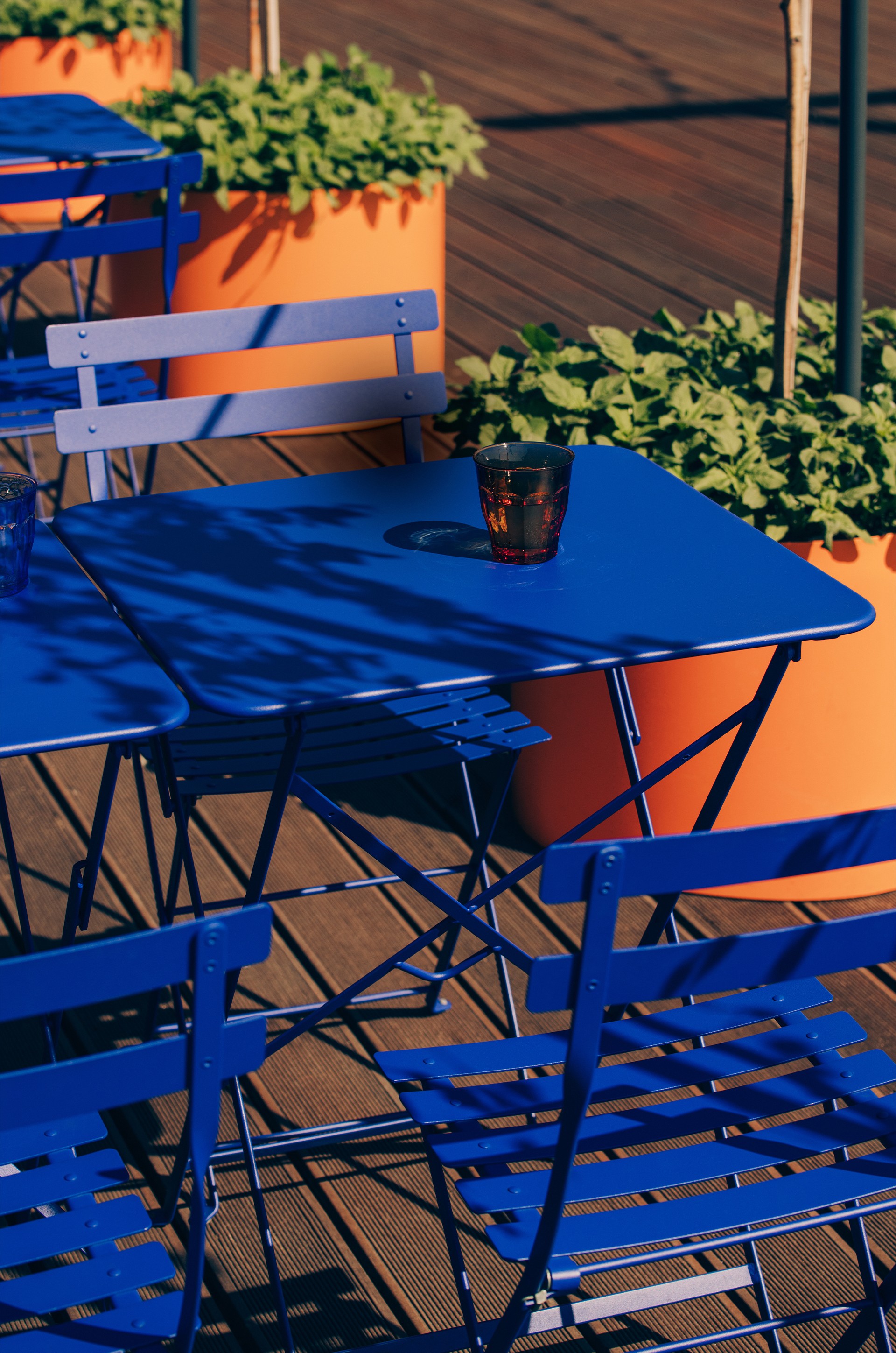 Blue folding bistro tables and chairs with orange planters on a wooden terrace, Woda restaurant brand colours