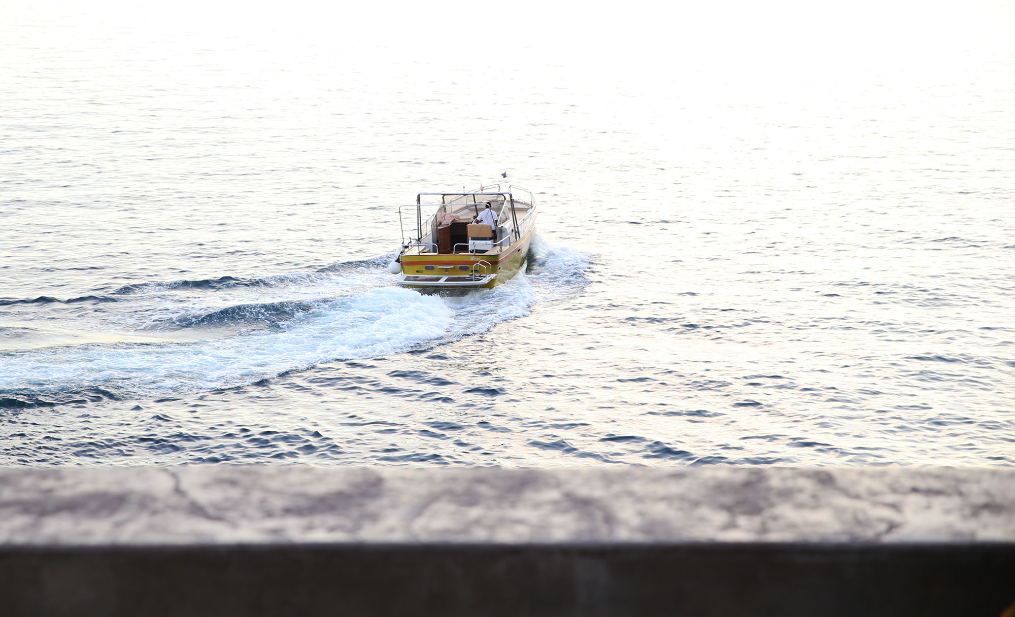 Small motorboat trailing a wake as it heads out to sea at sunset
