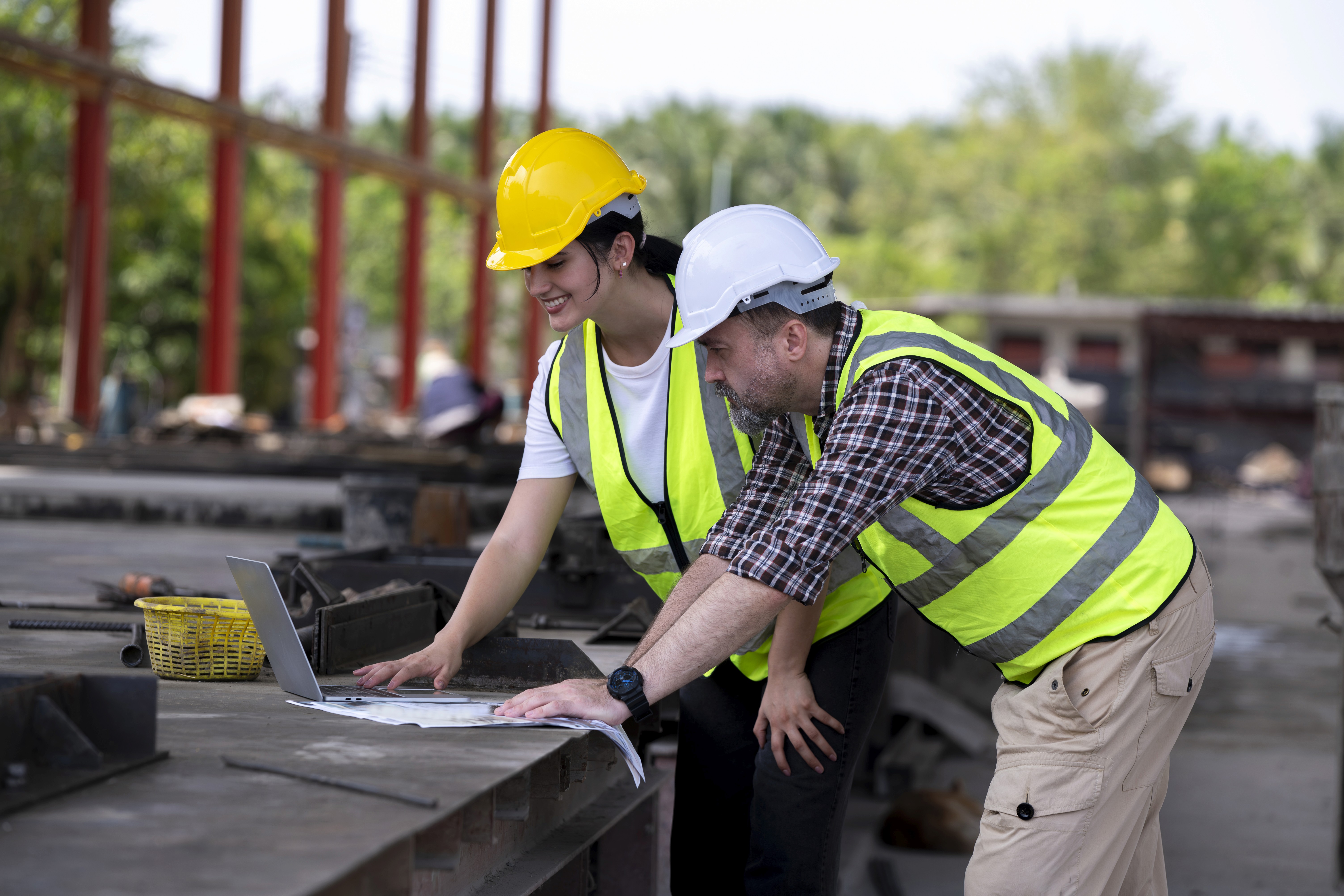 Two engineers in helmets leaning over a table in mid discussion.
