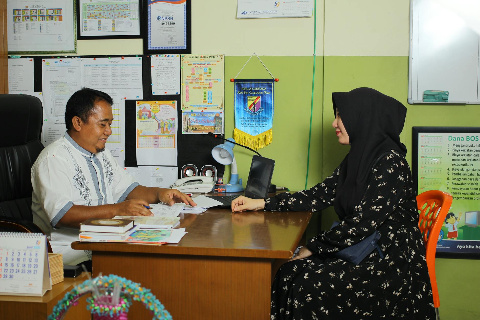 A parent and a school administrator sit at a round table reviewing a thick folder of academic assessment papers.
