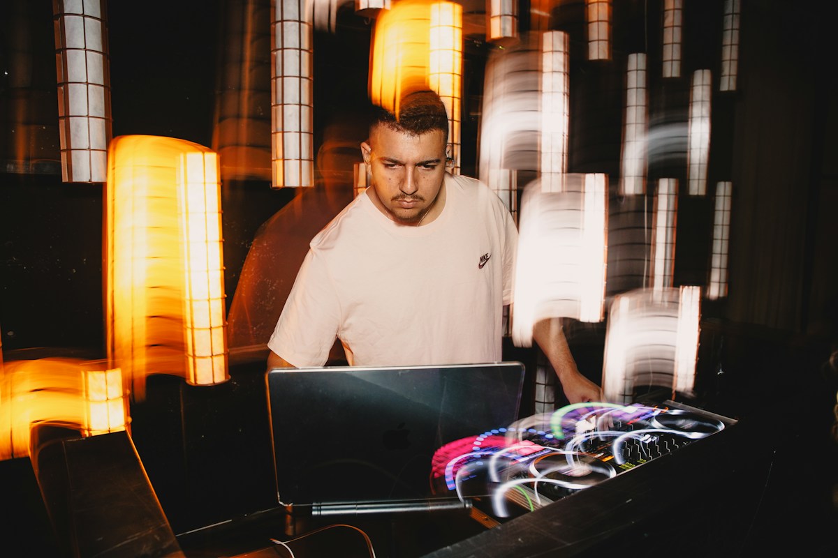 DJ arbejder ved laptop og mixer i et oplyst festlokale