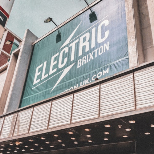 Large outdoor sign reading "Electric Brixton" with a website URL on a building facade under streetlights.