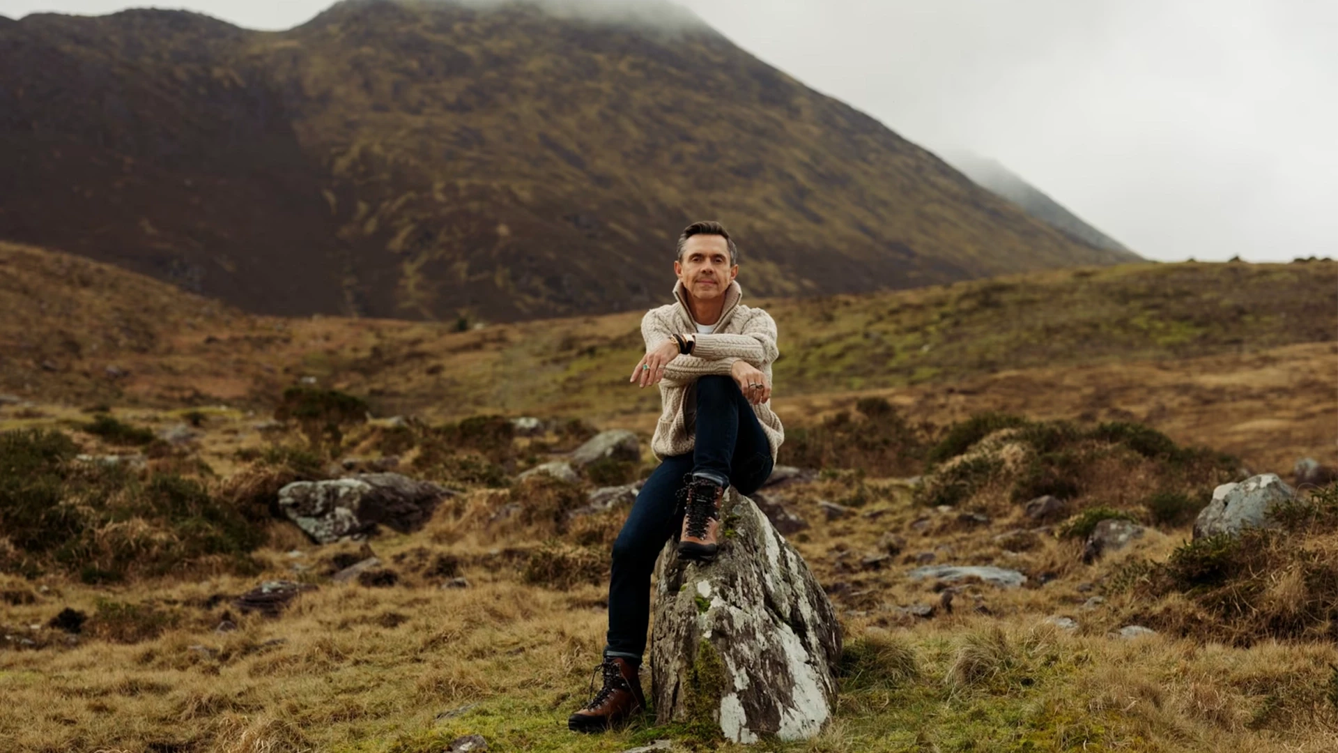 Editorial profile photo of Shaun Leane sitting casually on a rock in a vast Kerry mountain landscape, featured in the Financial Times.