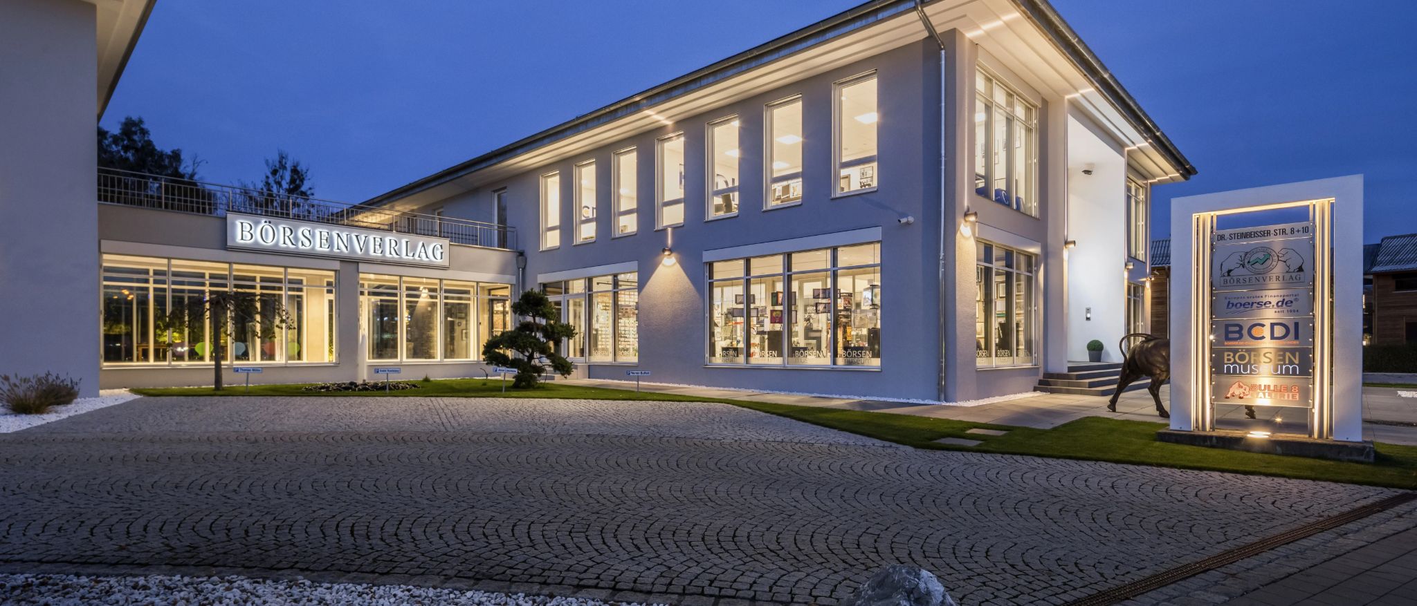 Gebäude des TM Börsenverlags Rosenheim bei Abendbeleuchtung.