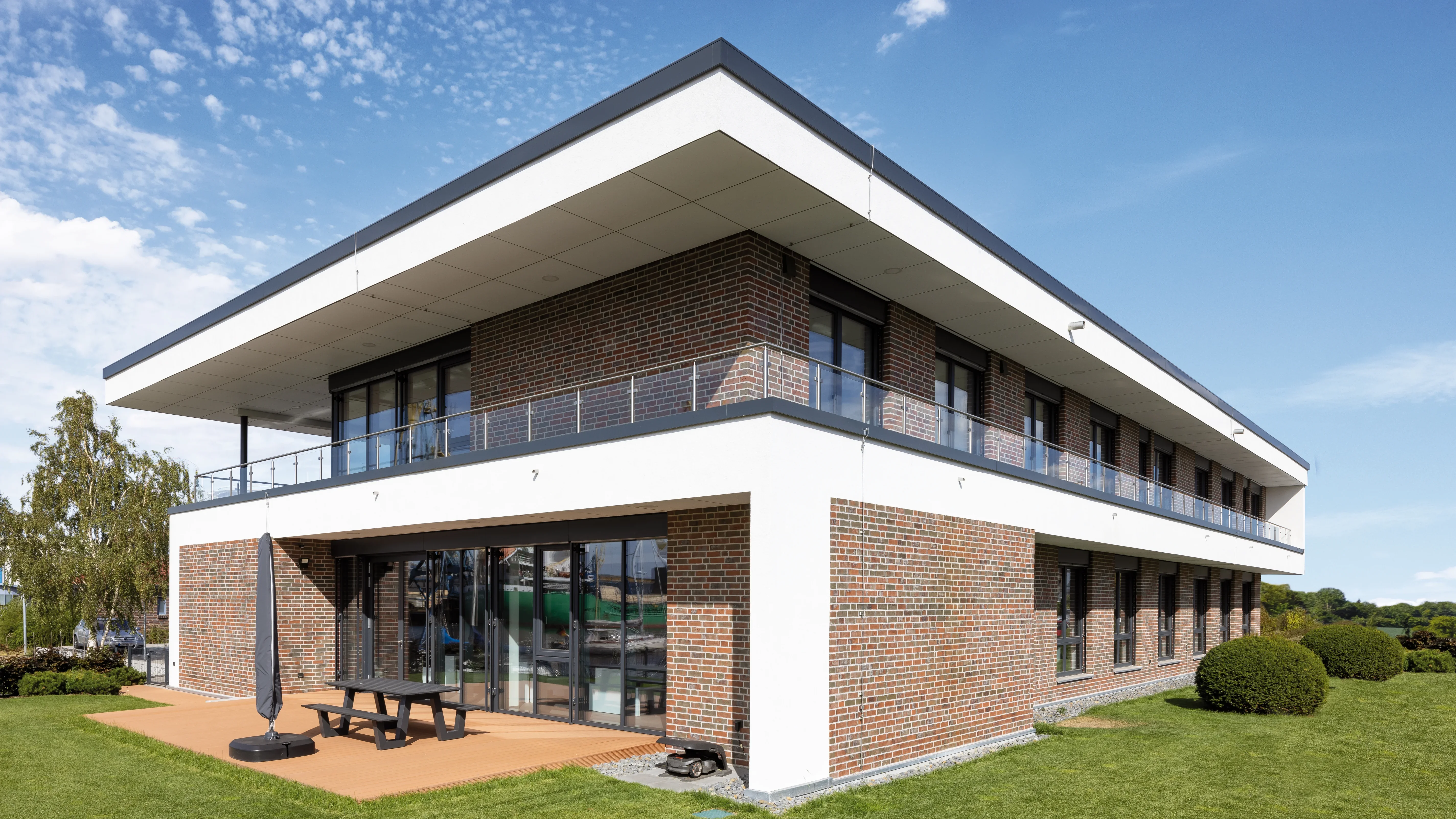 Rechteckiges Einfamilienhaus mit Klinkerfassade, moderner Architektur und großflächiger Glasfront an sonnigem Tag.