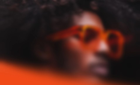 Blurred close-up portrait of a person wearing orange sunglasses against an orange background