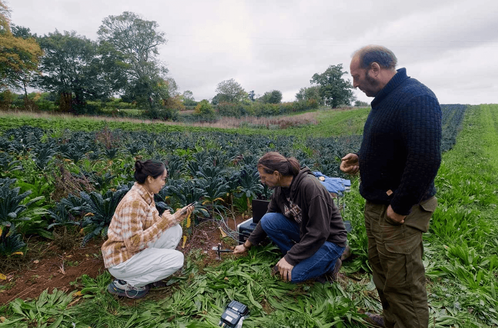 Lady in green overalls in a field doing an experiement