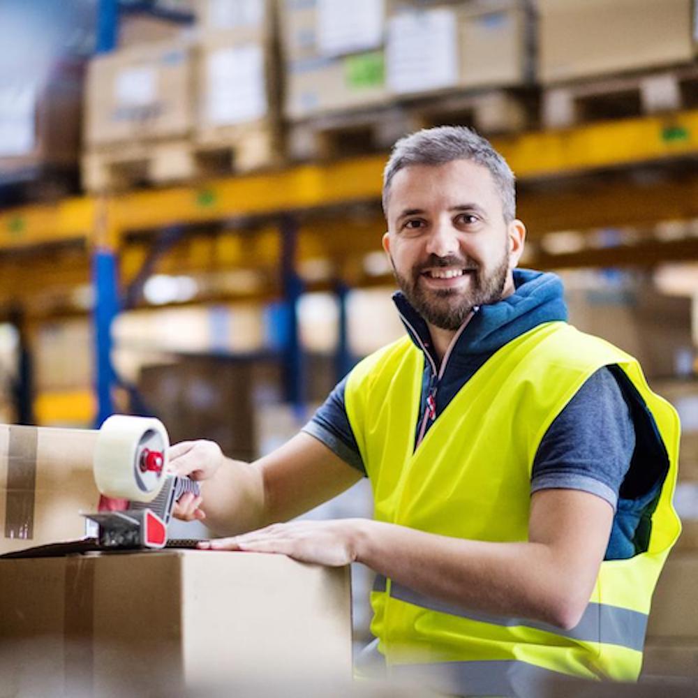 A person in a hi-viz jacket packing a box in a warehouse