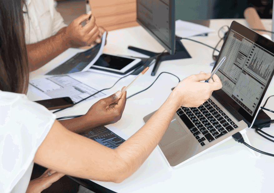 Nahaufnahme eines Schreibtischs mit zwei Laptops und gestikulierenden Armen zweier Personen