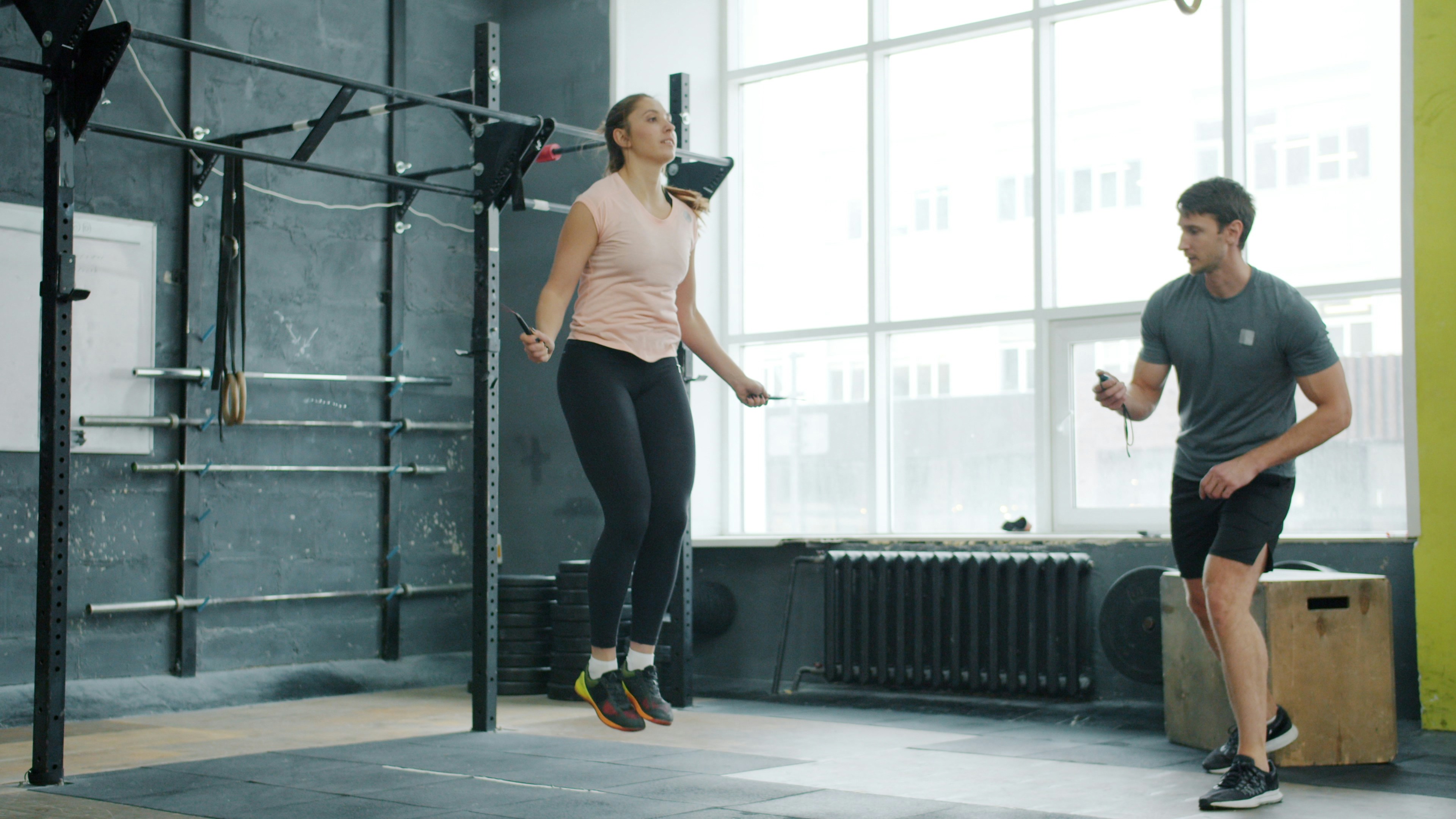 Woman jumps rope while man watches in gym.